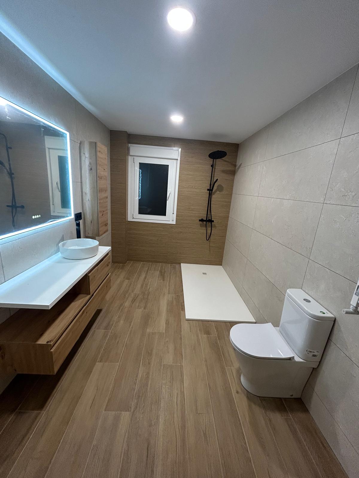 Baño reformado con suelo imitación madera, plato de ducha y espejo retroiluminado