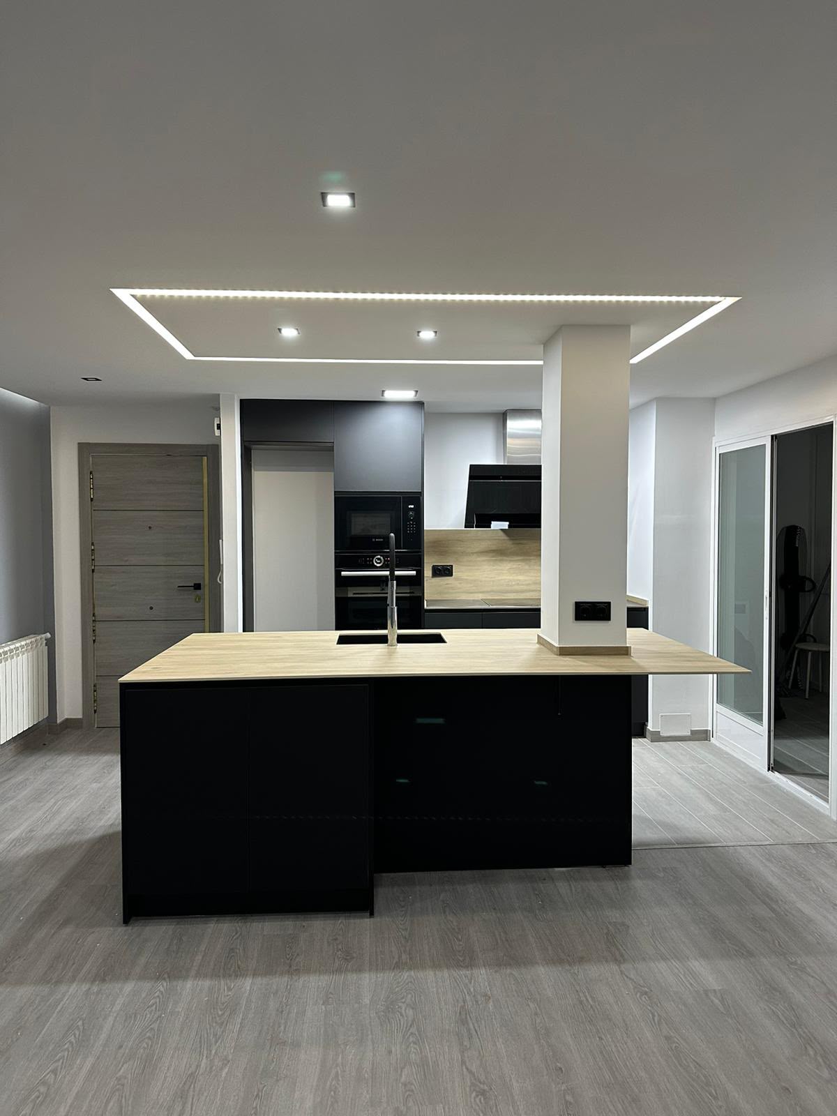 Cocina reformada por RenovaHome con isla central, encimera de madera y frentes negros mate