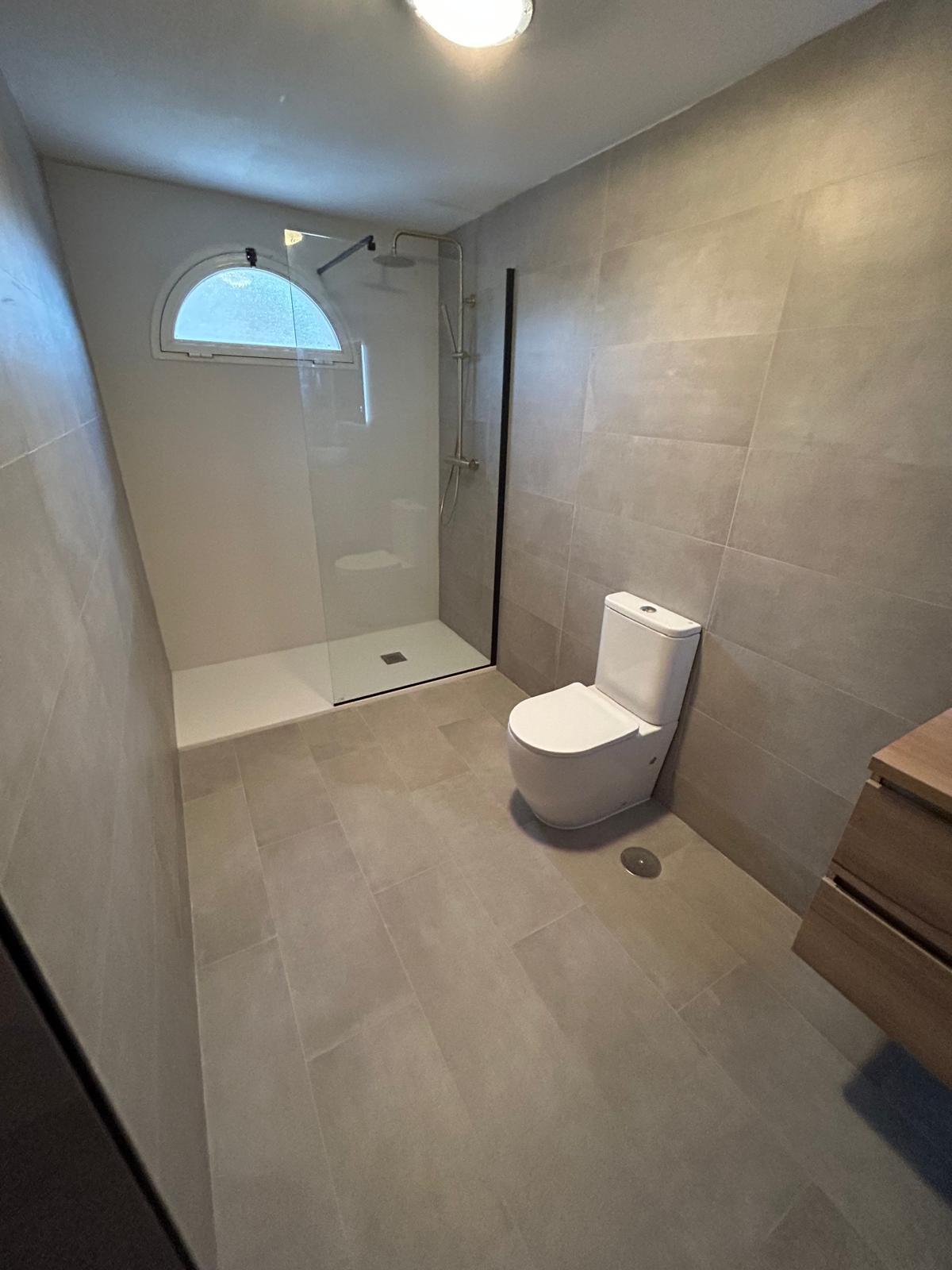 Baño reformado con ducha enrasada, mampara de cristal y porcelánico gris