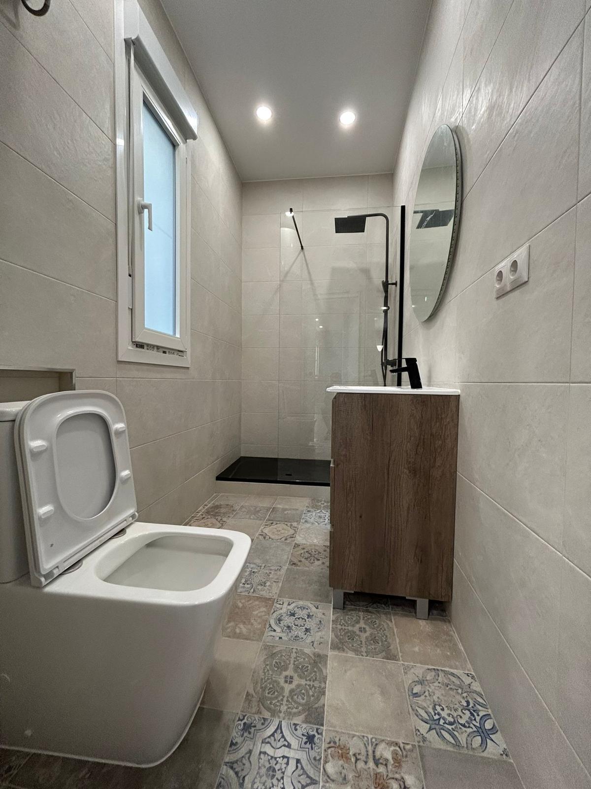 Baño reformado con ducha de obra, mueble de madera y suelo hidráulico